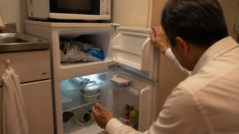 冷凍冷蔵庫を開けて少ない食材を確認する50代一人暮らし男性の後ろ姿