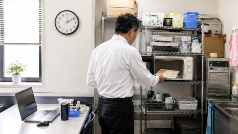 職場の給湯室で電子レンジから昼食を取り出す50代男性の後ろ姿