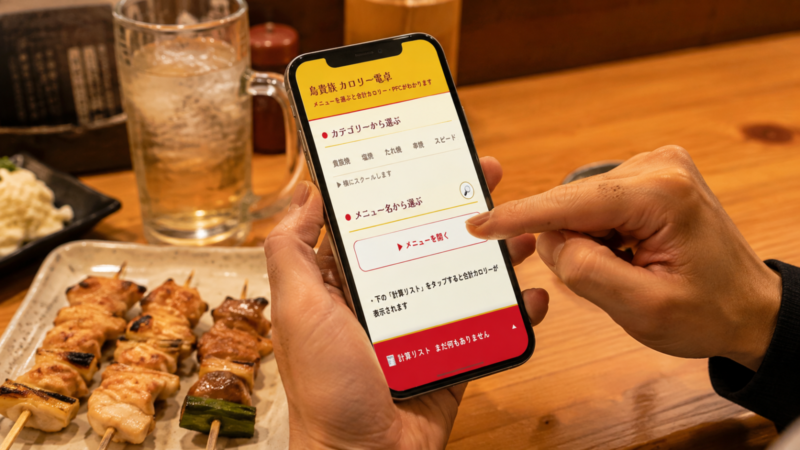 鳥貴族のテーブルでスマホの「鳥貴族 カロリー電卓」を操作し、メニューを選んでいる手元